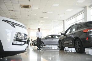 joven africano americano coche concesión principal en pie en vehículo sala de exposición foto