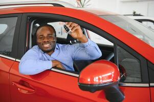 Feliz comprador de vehículo africano dentro de su auto nuevo con la llave del auto foto