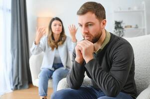 Pareja discutiendo. esposa gritos a su desesperado marido sentado en un sofá en el vivo habitación a hogar foto