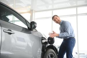 Young man buying first electric car in the showroom. Eco car sale concept photo