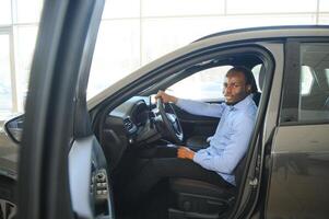 Car Owner. Joyful Afro Guy Smiling, Sitting In New Automobile Driving From Dealership Shop photo