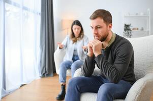 Family quarrel, man and woman sitting on sofa at home. angry woman yells at her husband photo