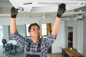 Portrait of young male indian technician repairing air conditioner. Air conditioner repairs. photo