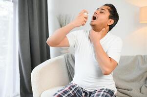 Indian man sick at home, cold, flu. A man uses a throat spray photo