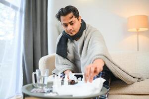 Portrait of sick Indian man with runny nose holding paper napkins near face sitting at home. Flu, virus, allergy concept photo