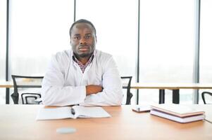 africano médico sentado cansado a el mesa en el hospital foto