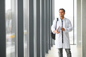 Portrait of a young Indian male medical student in a white coat waving photo