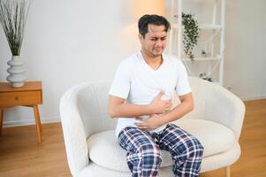 Sad exhausted guy of indian and arabian ethnicity, holds his hands on his stomach, grimaces from pain in his stomach, suffers from poisoning, spasm, stomach problems photo