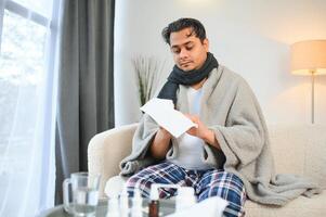 Portrait of sick Indian man with runny nose holding paper napkins near face sitting at home. Flu, virus, allergy concept photo