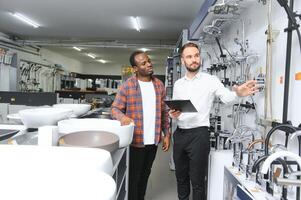 Young african man choosing faucets standing with salesman near the showcase of plumbing shop photo