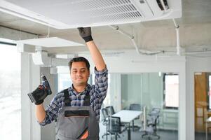 Concentrated young Indian engineer setting up air conditioner. photo