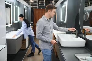 Young couple choosing new bathroom furniture at the plumbing shop with lots of sanitary goods photo