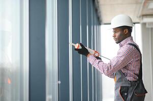 Construction african worker repairing plastic window with screwdriver indoors, space for text. Banner design photo