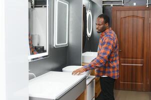africano americano a el edificio mercado mirando para lavabo dentro su baño foto