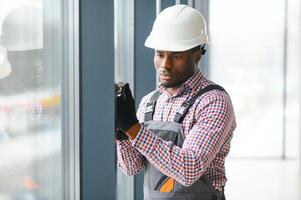 Low Angle View Of A Young African Repairman In Overalls Installing Window photo