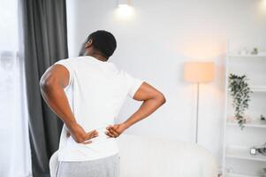 African American guy suffering from back pain, leaning on sofa, cannot walk at home photo