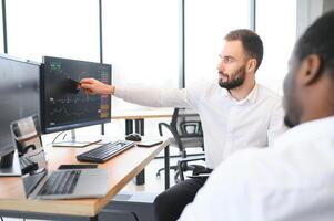 Two men colleagues traders sitting at desk at office monitoring stock market photo