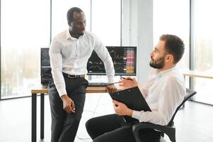 Two diverse crypto traders brokers stock exchange market investors discussing trading charts research reports growth using pc computer looking at screen analyzing invest strategy, financial risks photo