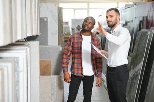 African man choosing ceramic tiles and utensils for his home bathroom and male seller helps him to make right decision photo