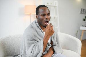 Sick african man using throat spray at home photo