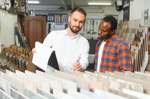 African man choosing ceramic tiles and utensils for his home bathroom and male seller helps him to make right decision photo