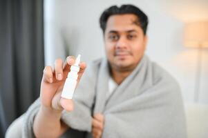 A sick Indian is treated at home and uses a nasal spray. Healthcare concept photo