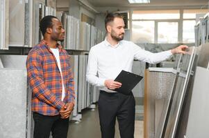 African man choosing ceramic tiles and utensils for his home bathroom and male seller helps him to make right decision photo