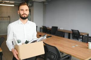 Young handsome businessman in light modern office with carton box. Last day at work. Upset office worker is fired photo