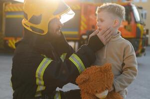 A firefighter take a little child boy to save him. Fire engine car on background photo