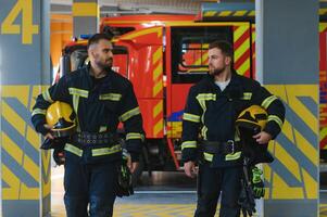 Two firefighters in protective clothing in helmets with fire engine photo