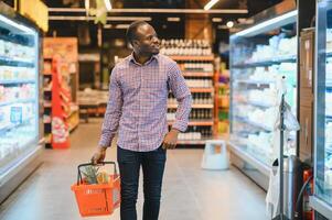 African man shopping at supermarket. Handsome guy holding shopping basket photo