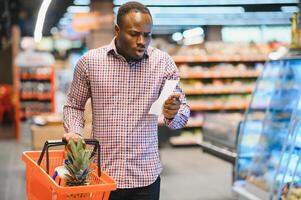 African man shopping at supermarket. Handsome guy holding shopping basket photo