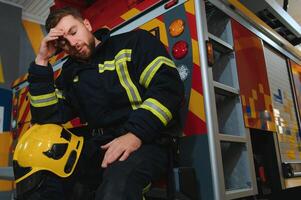 un sentado y transpiración bombero es exhausto, afligido y cansado después siendo abrumado en un rescate operación foto