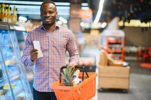 African man shopping at supermarket. Handsome guy holding shopping basket photo