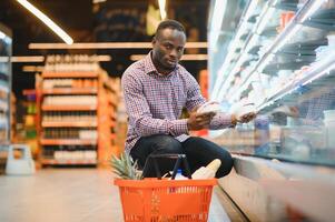 africano hombre compras a supermercado. hermoso chico participación compras cesta foto