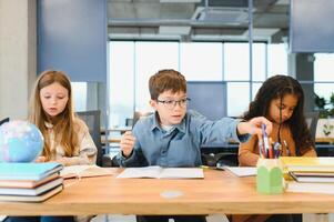 Focused multiracial students kids writing down data into notebook while sitting at table photo