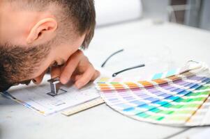 Print house worker controlling printing process quality and checking colors with magnifying glass photo