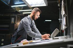 Print house worker controlling printing process quality and checking colors with magnifying glass photo