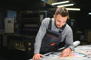 Print house worker controlling printing process quality and checking colors with magnifying glass photo