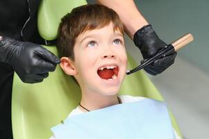 pequeño chico se sienta en del dentista silla en bueno estado animico después dental procedimientos. joven paciente con sano dientes foto