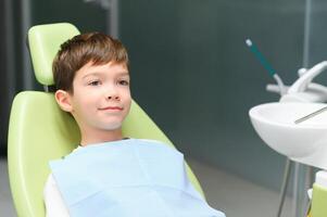 pequeño chico se sienta en del dentista silla en bueno estado animico después dental procedimientos. joven paciente con sano dientes foto