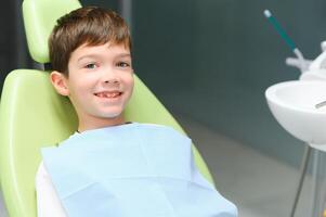 pequeño chico se sienta en del dentista silla en bueno estado animico después dental procedimientos. joven paciente con sano dientes foto