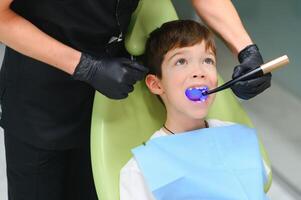 A little boy having his tooth done in the clinic - putting the photopolymer lamp with blue light in the mouth photo