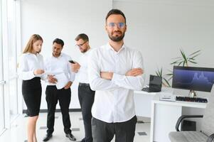 Team leader stands with coworkers in background photo