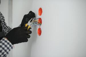 Electrician Builder at work, installation of sockets and switches. Professional in overalls with an electrician's tool. Against the background of the repair site photo