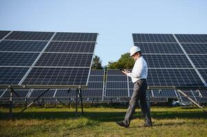 Industrial senior man engineer walking through solar panel field for examination photo