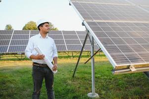 retrato joven indio técnico o gerente vistiendo formal paños en pie con solar panel. renovable energía, hombre en pie cruzado brazo, Copiar espacio foto