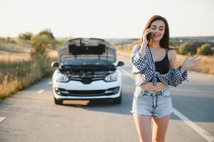 The young girl broke the car and she opened the hood and tried to repair the car on the road. A woman calls on a smartphone with a car evacuation service photo