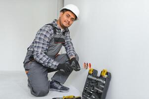 un indio electricista instala un toma de corriente en un nuevo edificio foto