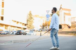 joven hermoso cegado hombre caminando con palo en pueblo foto